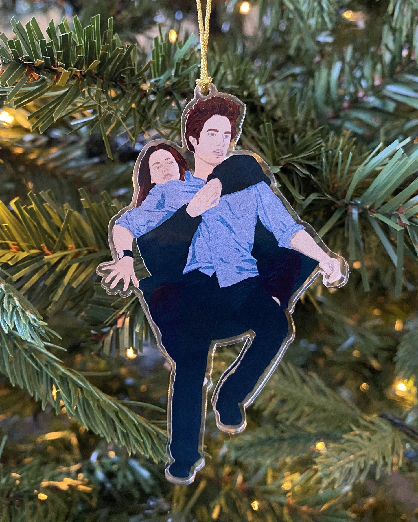 A Twilight inspired Christmas tree ornament featuring an illustration of Edward Cullen and Bella Swan, hanging on a Christmas tree with a gold cord.